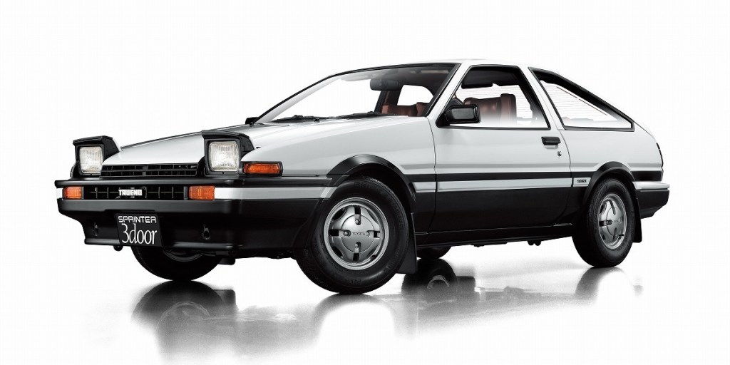 The image shows a white and black early 1980s Toyota sports coupe with pop-up headlights.